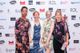 lt text: Deborah Husbands, Lindsay Bywood, Alison Eardley and Hannah Thompson are standing in front of a wall of logos. They are all dressed smartly for an awards show and smiling. Hannah is holding her white cane in one hand.
